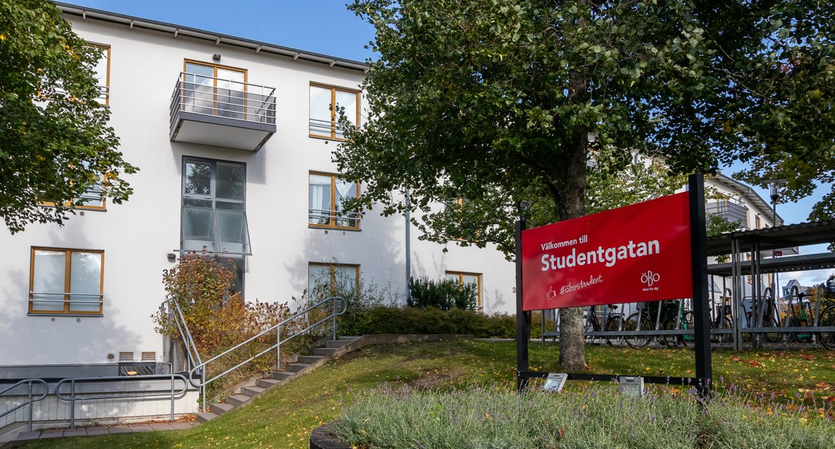 Exteriör av ett vitt flerbostadshus med skylt som visar ”Välkommen till Studentgatan”.